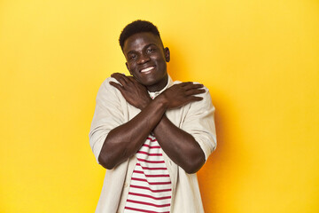 Stylish young African man on vibrant yellow studio background, hugs, smiling carefree and happy.