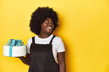 Baking woman with cake, a sweet treat prepared points with thumb finger away, laughing and carefree.