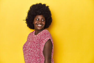 African-American woman with afro, studio yellow background looks aside smiling, cheerful and pleasant.