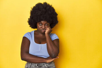 Fototapeta na wymiar African-American woman with afro, studio yellow background who feels sad and pensive, looking at copy space.