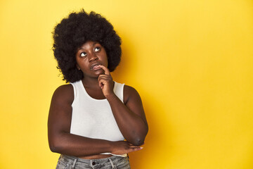 Fototapeta na wymiar African-American woman with afro, studio yellow background looking sideways with doubtful and skeptical expression.