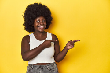 African-American woman with afro, studio yellow background excited pointing with forefingers away.