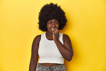 Fototapeta na wymiar African-American woman with afro, studio yellow background biting fingernails, nervous and very anxious.
