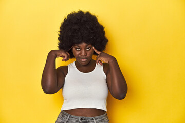 African-American woman with afro, studio yellow background focused on a task, keeping forefingers...