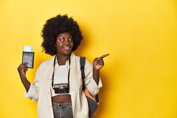 Travel-ready African-American woman holding an airplane ticket on a yellow background.