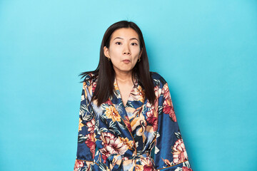 Elegant young Asian woman in kimono, studio shot shrugs shoulders and open eyes confused.