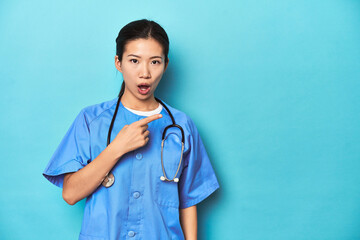 Asian nurse with stethoscope, medical studio shot, pointing to the side