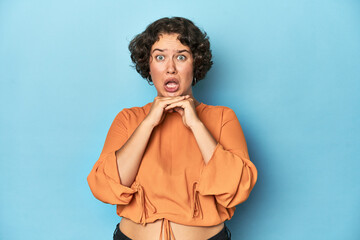 Young Caucasian woman with short hair praying for luck, amazed and opening mouth looking to front.