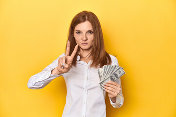 Redhead with dollar bills, cash in hand showing number two with fingers.