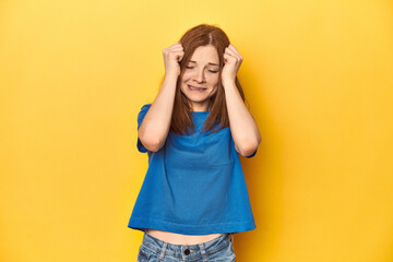 Redhead in blue t-shirt on yellow backdrop crying, unhappy with something, agony and confusion concept.