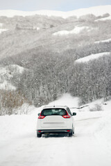White car riding on a snow-covered road in the European Alps while a snowstorm. Drifts and snow drifts during a snowfall.