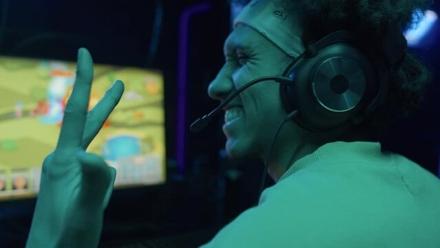 Close-up shot of young African American man and anonymous friend playing fun anime cartoon style strategy video game in cyberclub together, scoring, bumping fists and doing horns gesture