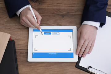 Electronic signature. Man using stylus and tablet at wooden table, top view