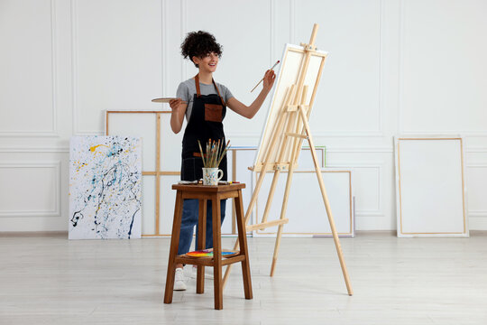 Young woman painting on easel with canvas in studio