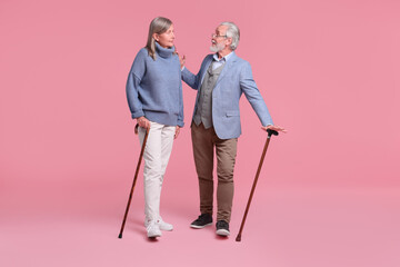 Senior man and woman with walking canes on pink background