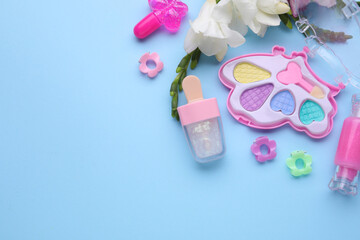 Decorative cosmetics for kids. Eye shadow palette, lipsticks, accessories and flowers on light blue...