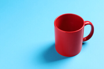 One red ceramic mug on light blue background, space for text