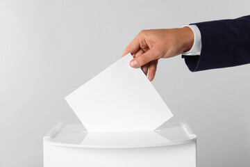 Man putting his vote into ballot box on light grey background, closeup