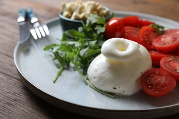 Delicious burrata cheese with tomatoes and arugula served on wooden table, closeup