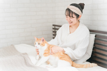 家のベッドルーム・寝室で猫・ペットを可愛がる飼い主の女性(首・のど・ゴロゴロ)
