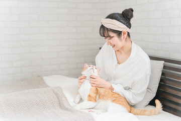 家のベッドルーム・寝室で猫・ペットを可愛がる飼い主の女性と飼い主を見る猫(スキンシップ)
