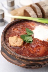 Tasty borscht with sour cream in bowl on light grey table, closeup