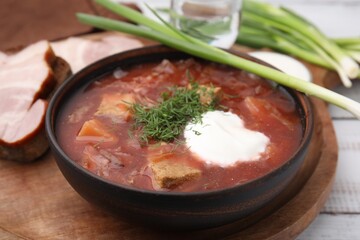 Tasty borscht with sour cream in bowl served with green onion on white wooden table, closeup