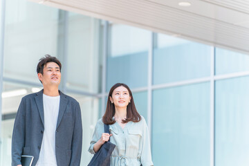 オフィスビルから出て話す男女（ビジネスマン・ビジネスウーマン・社内恋愛・社内結婚）
