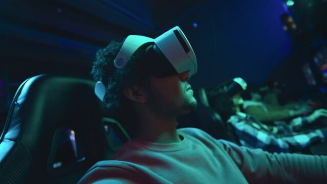 Medium close-up shot of Middle Eastern man putting on VR headset in cyber cafe to play first person shooter multiplayer game in simulated reality, and looking around