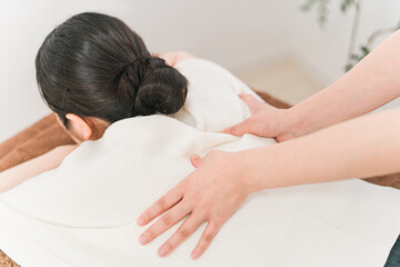 エステサロン・整体院で背中・肩をマッサージするマッサージ師・セラピスト・整体師・理学療法士の女性
