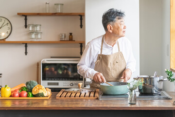 Fototapeta na wymiar 家のキッチンでフライパンを使って手料理を作るアジア人の高齢者男性（笑顔） 