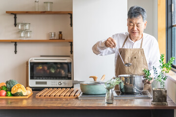 Fototapeta na wymiar 家のキッチンで料理を作って味見するアジア人の高齢者男性（笑顔） 