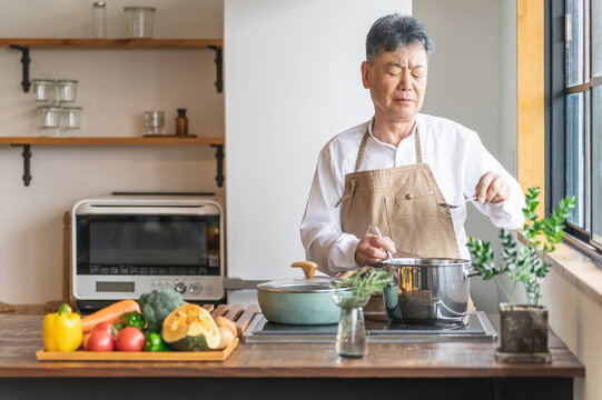 家のキッチンで料理を作るアジア人の高齢者男性（認知症・悩む）
