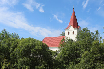 Fototapeta na wymiar Lutheran church with a red steeple and trees in front of it in Eglaine, Latvia