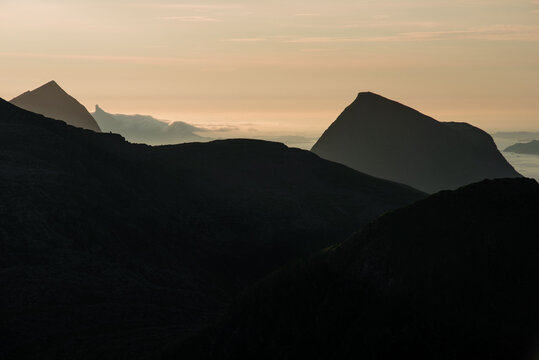 Mountain islands in Norwegian archipelago of Helgeland during sunset. Clouds forming on island mountain peaks at sea. Yellow sunset nordnorge. Dramatic contrast in Norway peaks. Smaltind, Lur&ouml;y fjell