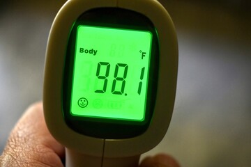 Hand holding a temporal thermometer with green digital reading in Fahrenheit 