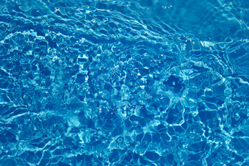 Blue water with ripples on the surface. Defocus blurred transparent blue colored clear calm water surface texture with splashes and bubbles. Water waves with shining pattern texture background.