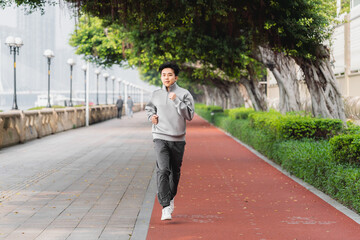 Asian man is running outdoors in the city park. 