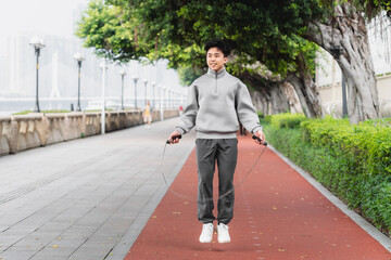 Asian sportsman is skipping rope outdoors in the city. 