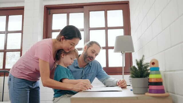 Happy parents and cute little son teaching homework and drawing a picture together at home. Happy caucasian family to spend time together to warmth at home. Family relationship concept.