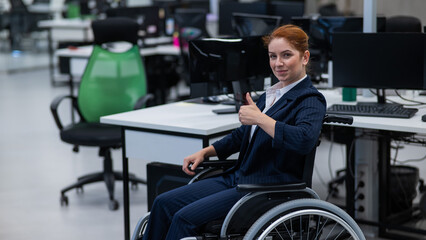 Fototapeta na wymiar Caucasian woman in wheelchair showing thumb up while sitting in open space office.