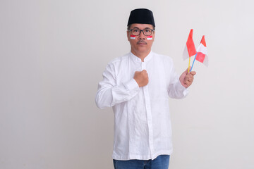 A man with red and white stickers on his cheeks is holding red and white flags, one hand on his...