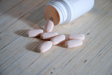 Fototapeta na wymiar A white container with pink pills in a wooden table