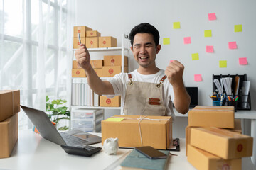 Young Asian businessman happy and excited after receiving new orders from SME customers. online marketing Entrepreneur packaging box, SME seller and independent online sales concept.