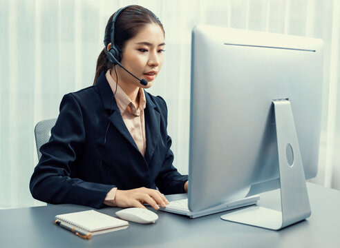 Asian call center with headset and microphone working on her laptop. Female operator provide exceptional customer service. Supportive call center agent helping customer on inquiry. Enthusiastic