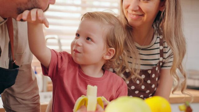 Happy Caucasian family eating banana together on counter in kitchen room at house