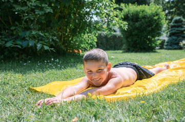 Cheerful boy playing in water slide in garden background trees