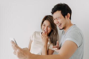 Funny couple asian lover laugh at the clip in the smartphone isolated on white. - obrazy, fototapety, plakaty