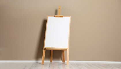 Wooden easel with blank board near beige wall indoors. Space for text
