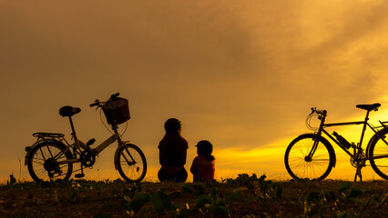 Silhouette biker lovely family sitting and talking at sunset over the ocean.  Mom and daughter...